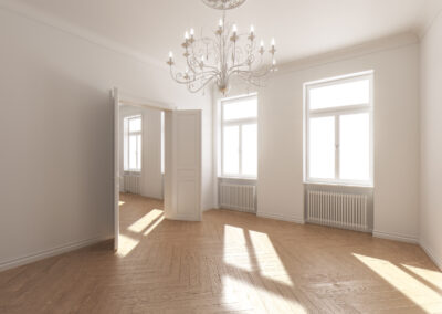 Zimmer ohne Einrichtung einer sanierten Wohnung in Wien. Fußboden und Türen aus Holz, weiß gestrichene Wände, Deckenluster in Kerzenoptik. Ein in weiß gehaltener und sehr heller Raum.